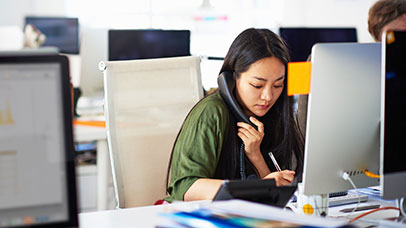 Woman working at a desktop and on the phone.