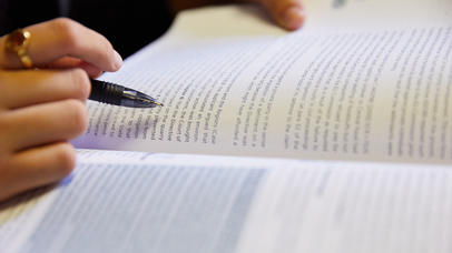Image of someone reading an open book using their pen as a line guide