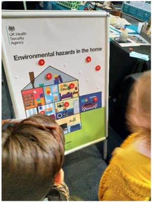 A poster board at an event stating 'Environmental hazards in the home' with a graphic of a cutaway of a house and the UK Health Security Agency logo