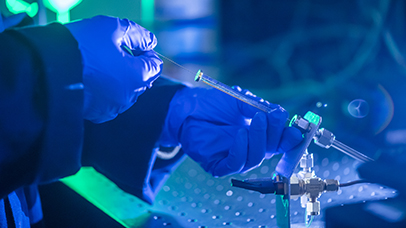 A syringe handled by a scientist's hands in surgical gloves