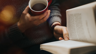 A person reading a book with a coffee.
