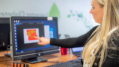 Photo of an academic pointing at a brightly-coloured image on a computer monitor