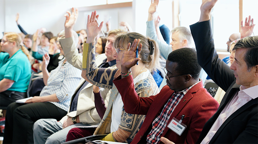 People sat in a packed out room all holding their hands up