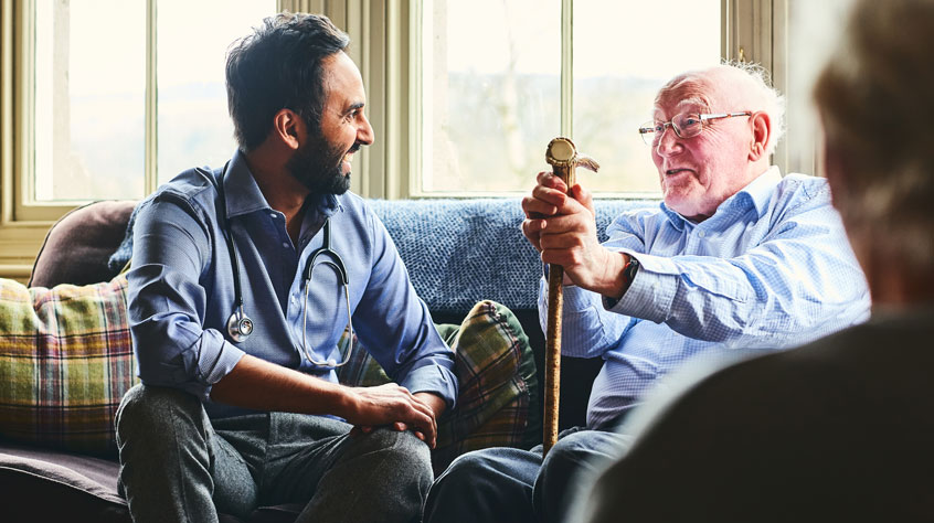 Healthcare professional sitting on a sofa with an older man, talking and laughing
