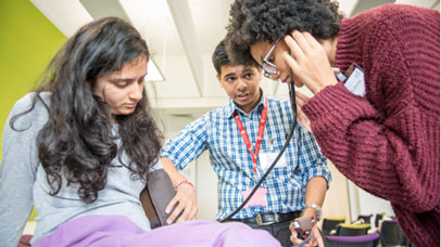 Person with a stethoscope, examining another person whilst a student observes 