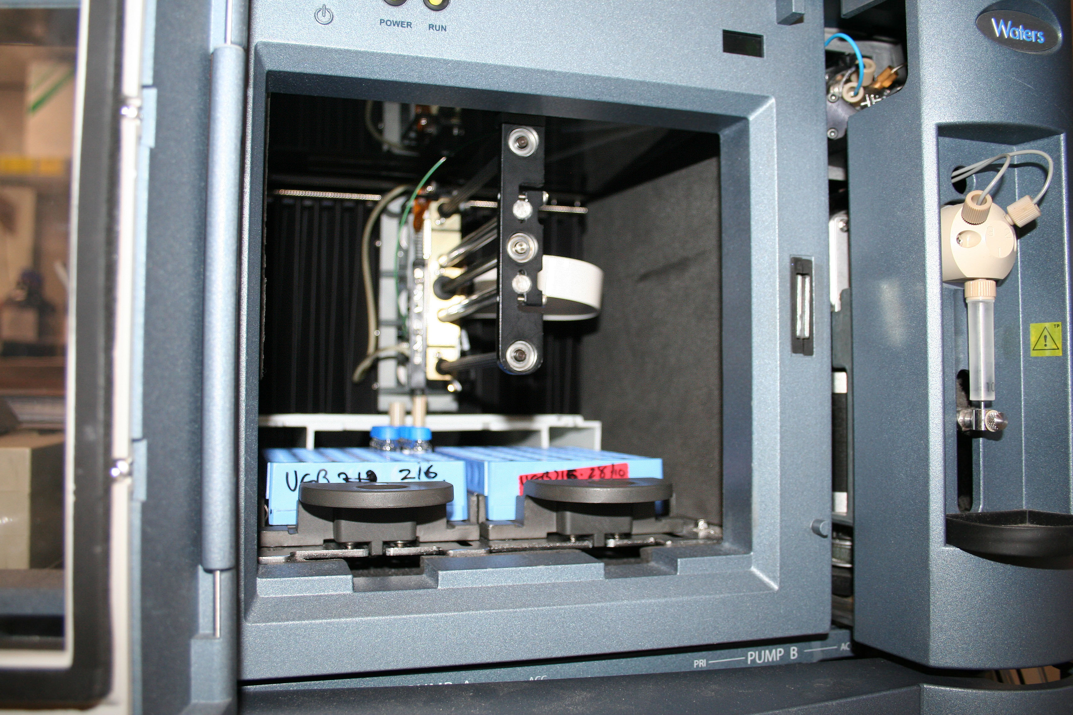 Close-up of a gray scientific instrument interior, showing intricate mechanical parts and labeled blue and red components, suggesting analytical functions.