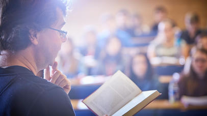 A lady reads a book at the front of a lecture hall