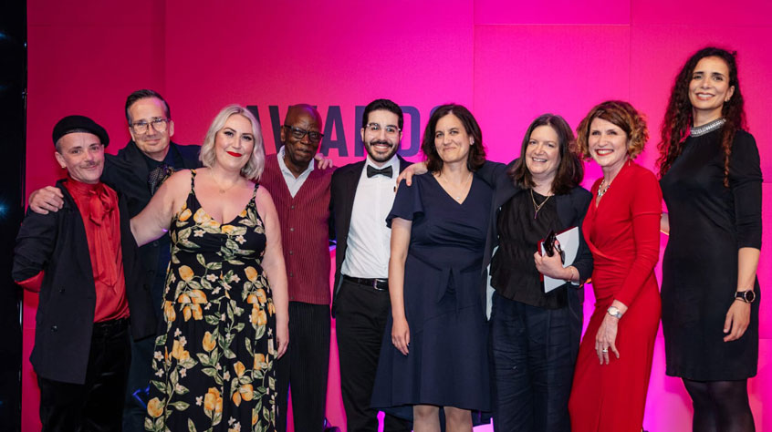 A group of people from the RCMG standing together in front of a bright pink background.
