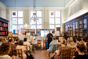A group of people sit on wooden chairs listening to 2 people present at the Launch of the guidance, taking place at Bishopsgate Institute Library.