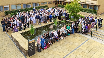 A large group of people is assembled outside at College Court. They are all looking at the camera which is high above them and some are waving. 