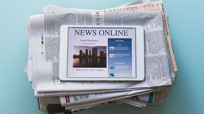 Tablet on top of a stack of newspapers, which reads: news online.