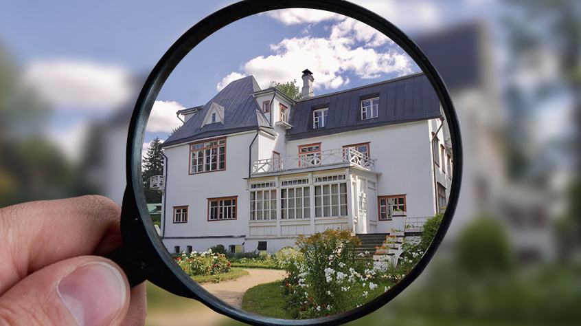A magnifying glass lens held up to bring the front of a large country house into focus