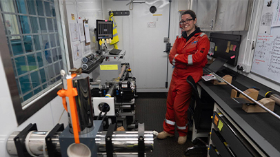 A woman in a red safety uniform stands beside a large machine, showcasing the facility's equipment.