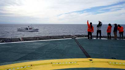 People waving to a ship on a large rig in the middle of the ocean.