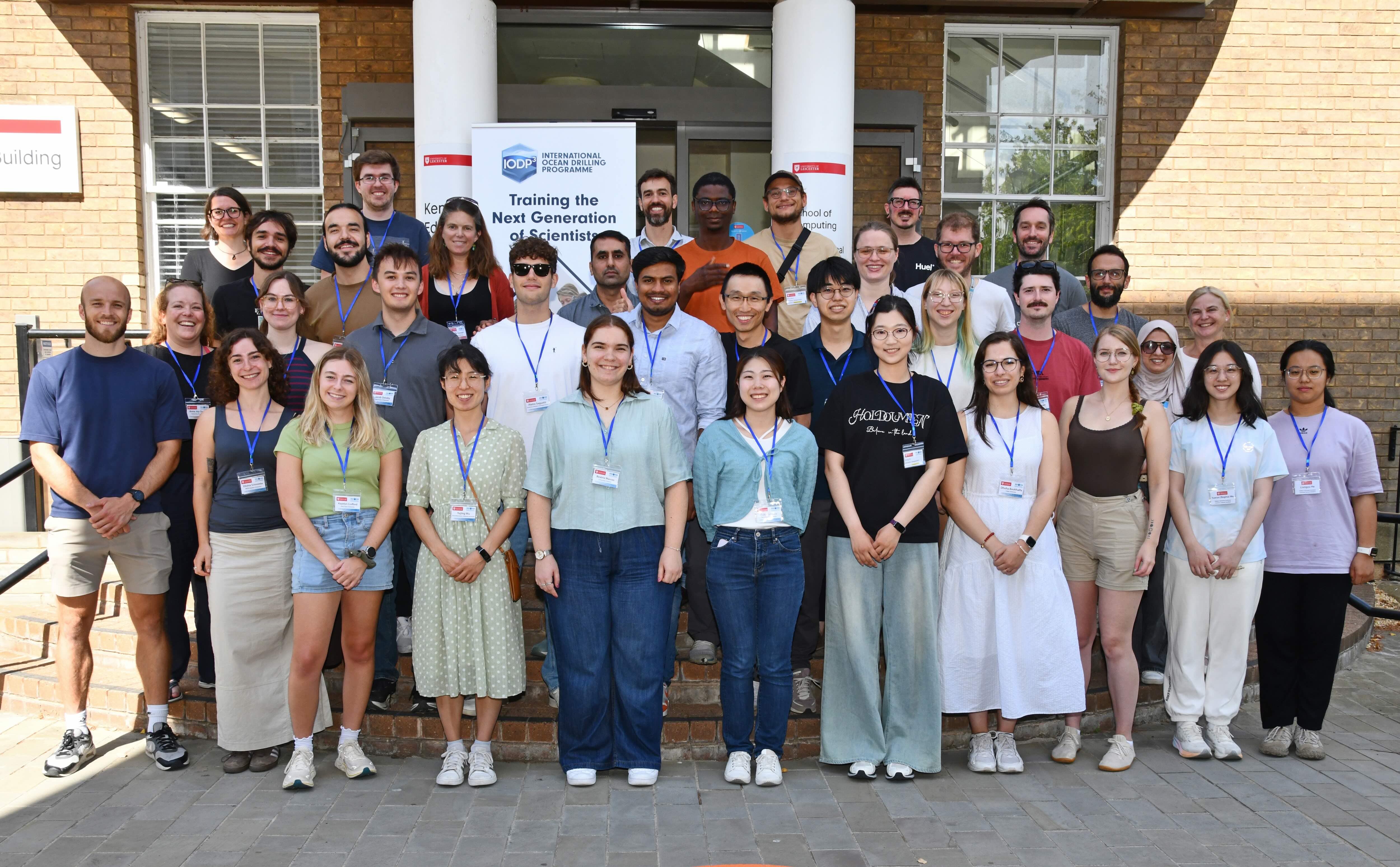 A numerous group of people from IODP stand and smile in front of the camera