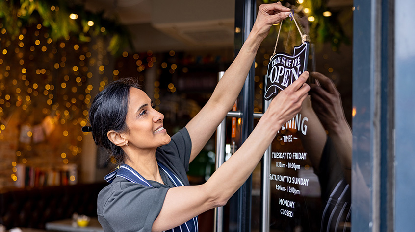 business owner hanging an open sign on the door at a cafe