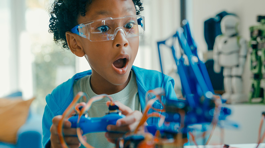 A young student showing excitement within a science laboratory, looks to be holding a console control pad