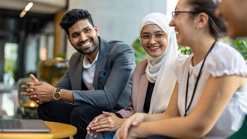 Three students or members of staff, sat at a table smiling and chatting