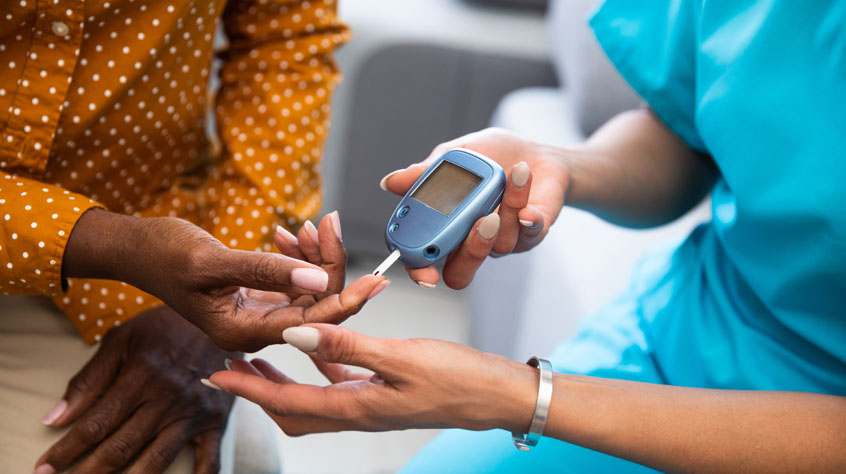 Young nurse doing a glucose blood test on her senior patient, during a home visit