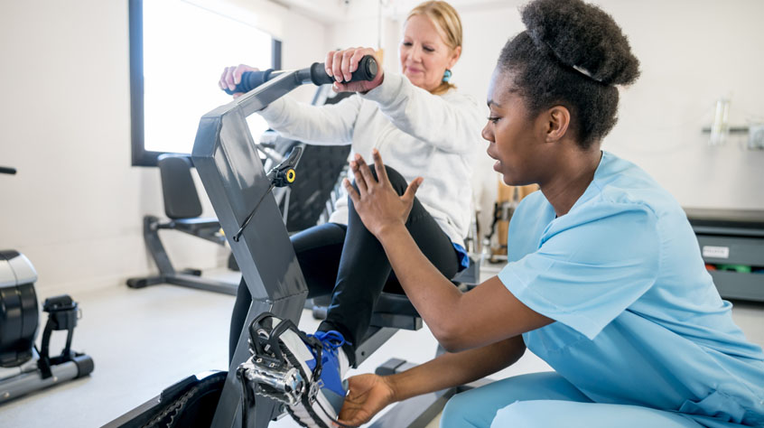 African american occupational therapist explaining a patient how to use the static bicycle and patient listening very careful