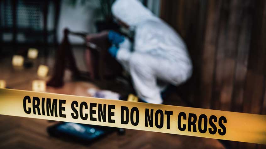 Forensic scientist at a crime scene with 'do not cross' tape