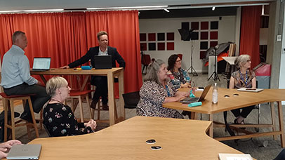 Six people are sat across three tables, their stare is focused to the side, as if watching a presentation off camera