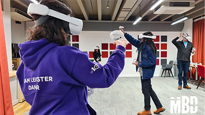 Four people wearing VR headsets and holding VR controllers frozen in various states of movement as they interact with what they are seeing through their VR headsets