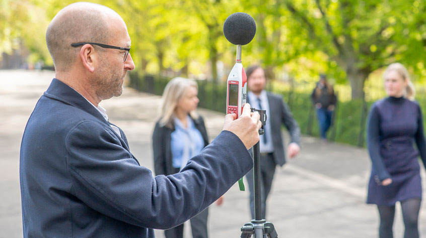 Person holding decibel reader as people walk past