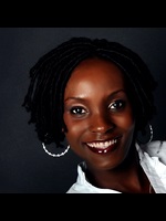 Dr Fiona Mulira smiles into the camera, she is wearing a white shirt and silver hoop earrings against a dark background