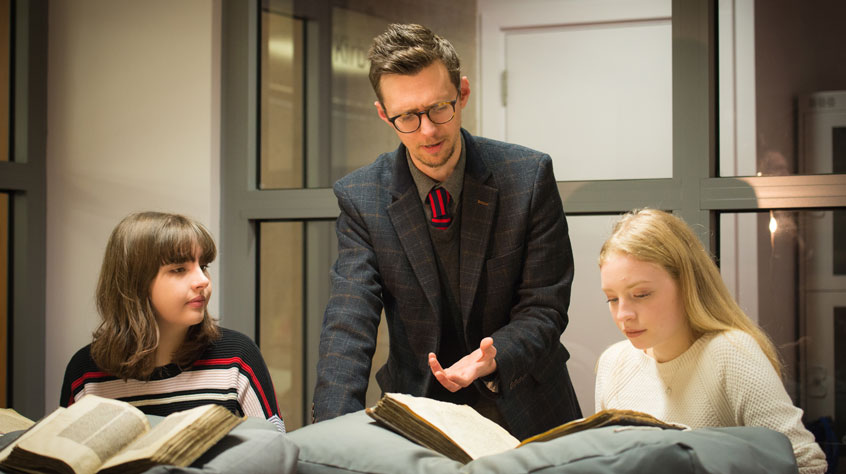 Two people reading from archives and an archivist speaking to them