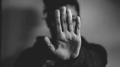 Image of a person with their hand out-streched, palm facing the camera, covering their face