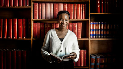 Law student standing in front of a law bookshelf, holding a book.