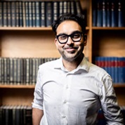 Neil Chakraborti posing for the camera in front of a large bookcase full of books