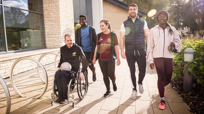 Student in a wheel chair walking with four of his colleagues 