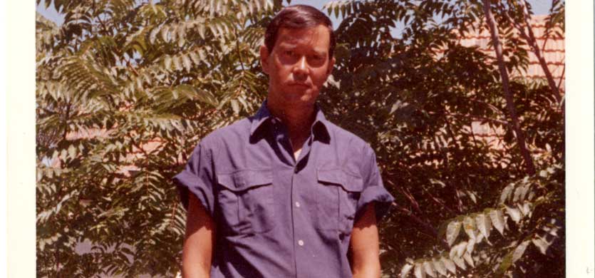 Joe Orton standing in front of some palm trees