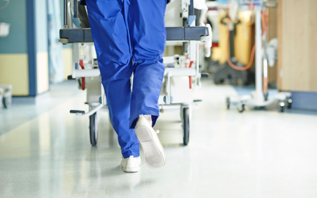 NHS worker in scrubs running with a gurney