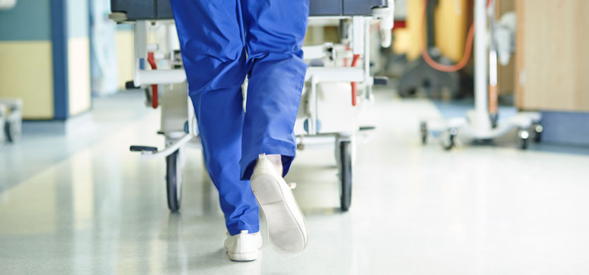 NHS worker in scrubs running with a gurney