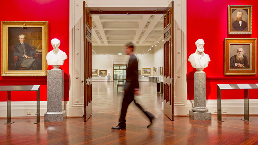 Man walking across two open doors at the front of a large room within a museum