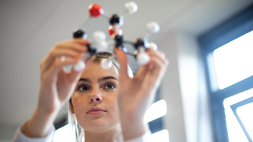 Female student holding up what looks to be a molecular structure made of spheres and dowels