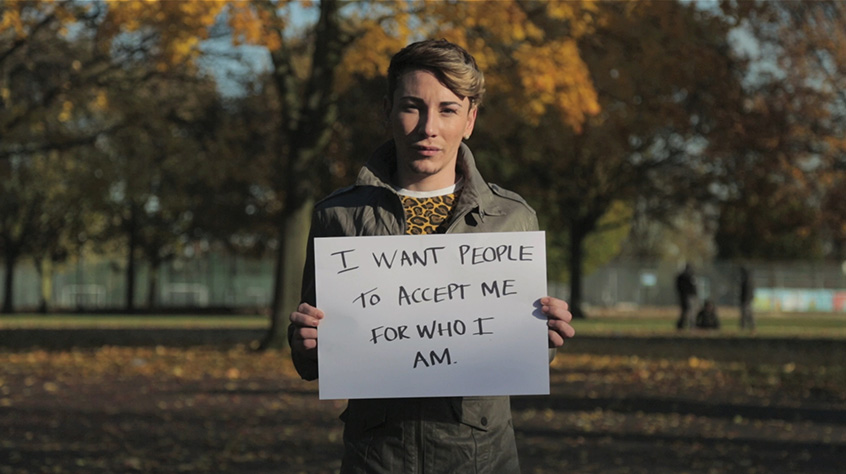 Person stood in front of trees with a sign that reads I want people to accept me for who I am