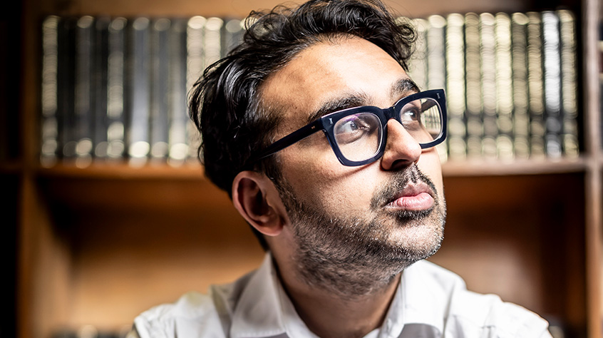 Professor Neil Chakraborti sat down looking up and to his left, a shelf of books sits behind him