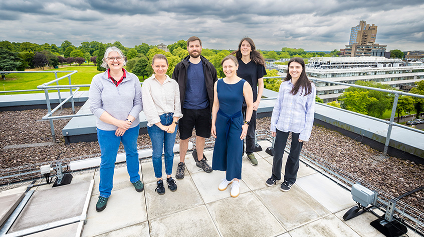 Students and staff stood on the roof of a building with other buildings within the University of Leicester campus displaying large in the background