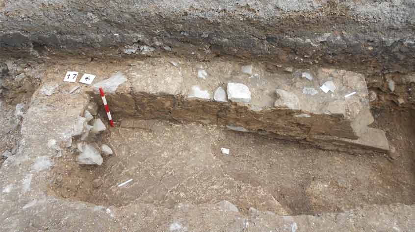 Part of a stone wall and floor survived in Trench 2 (E). Tile impressions can still be seen on the mortar floor bedding and the remains of a doorway can be seen to the right of the photograph.