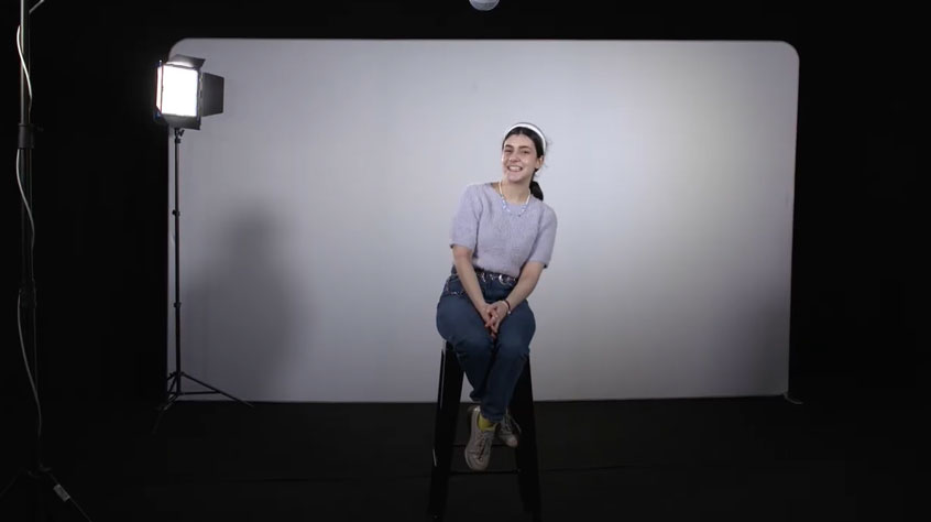 Woman sitting on a stool in front of a photography light and screen