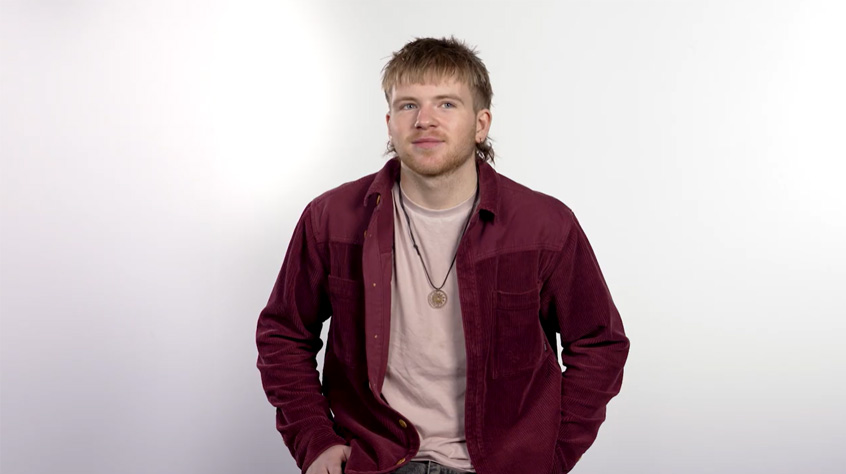 A young man sitting in front of a white background.