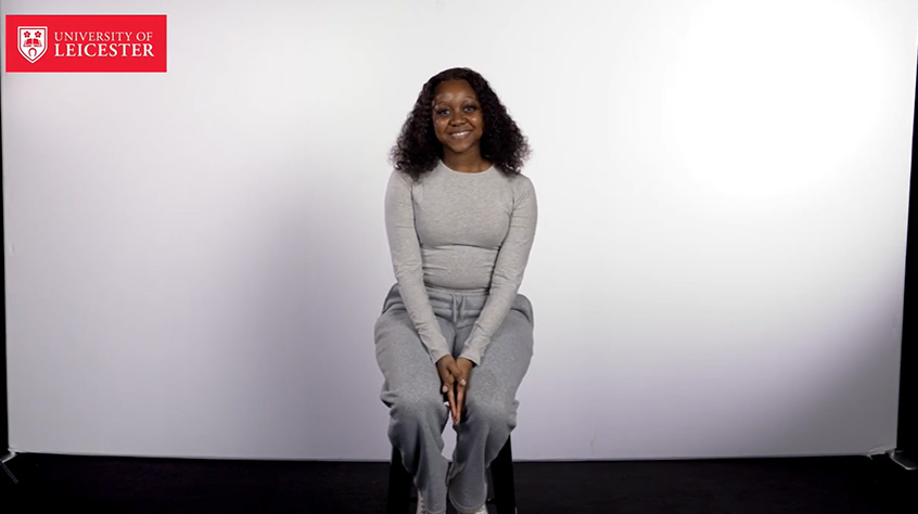 A woman seated on a chair against a plain white backdrop, looking directly at the camera.