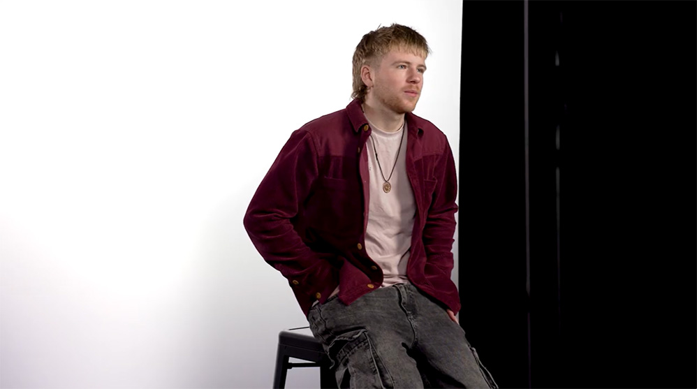 A young man sitting in front of a white background.