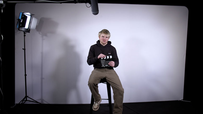 Student Jude sitting in a studio and holding a clapperboard.