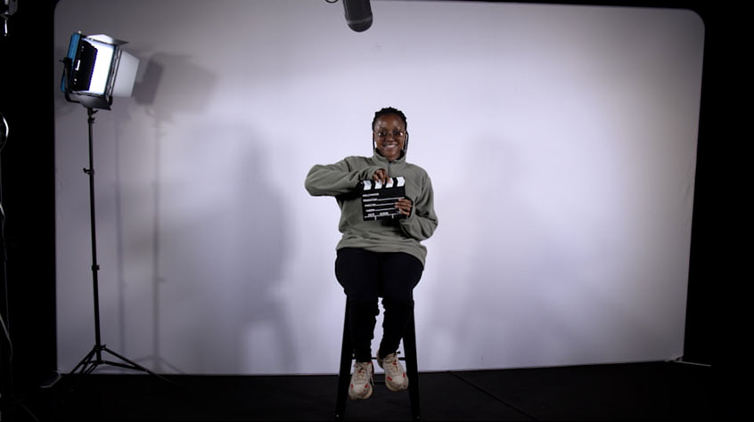 Student Natasha sitting in a studio and holding a clapperboard.