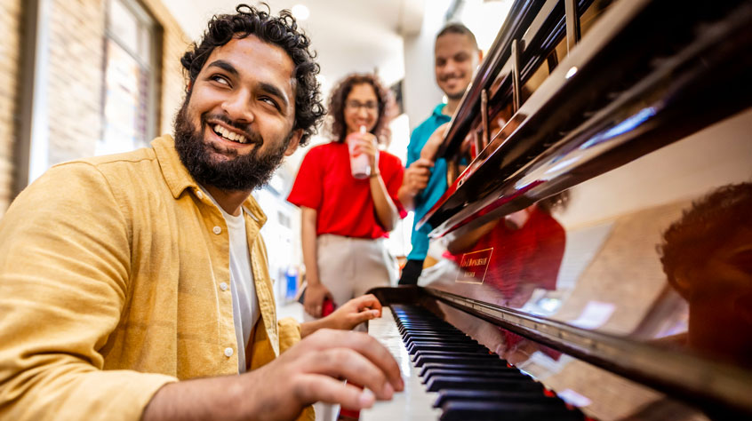 Student playing a piano whilst two other students look on